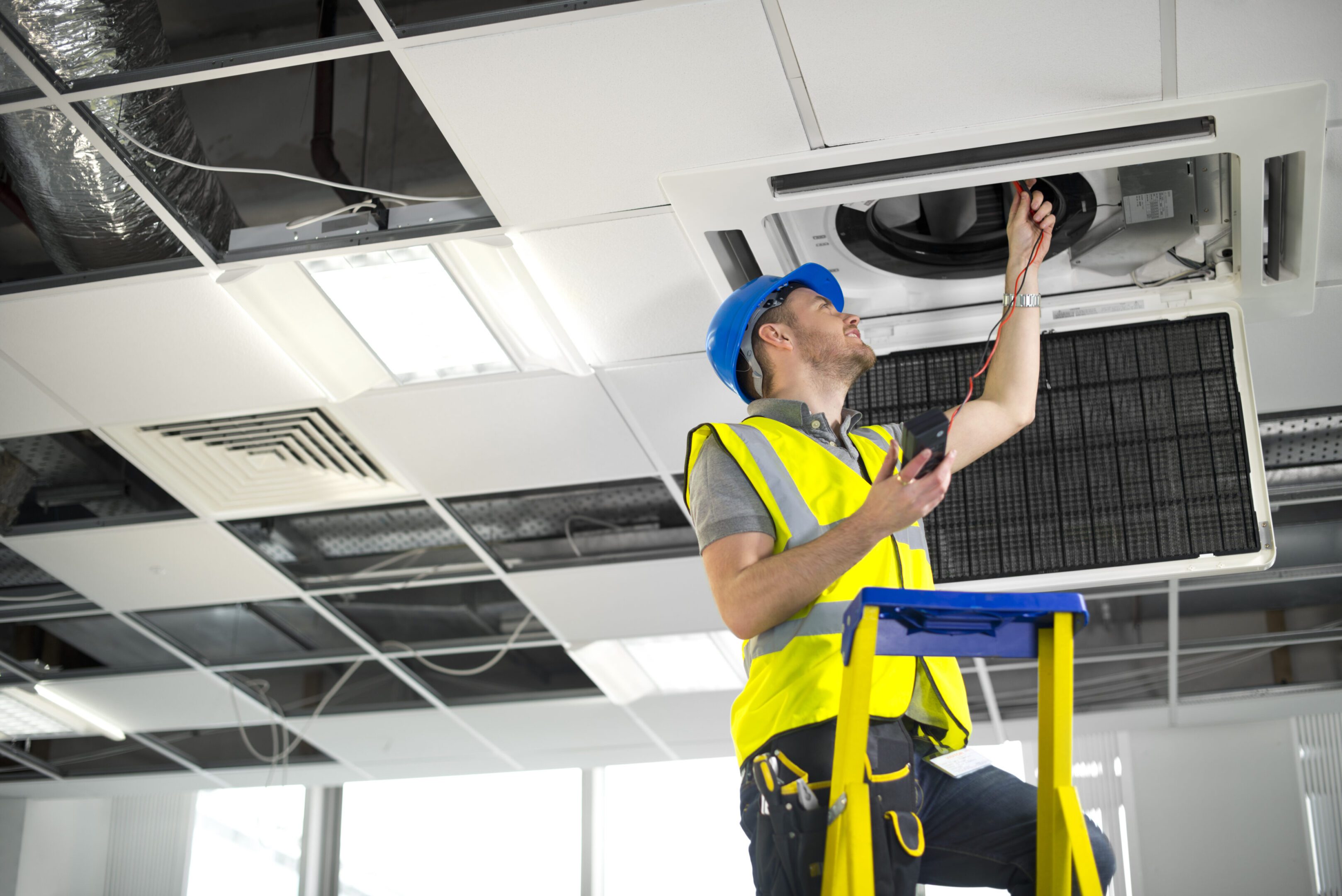 Worker inspecting ceiling air conditioning unit.